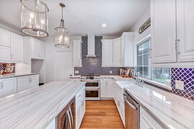 kitchen featuring stainless steel appliances, decorative backsplash, white cabinets, wall chimney range hood, and light stone counters