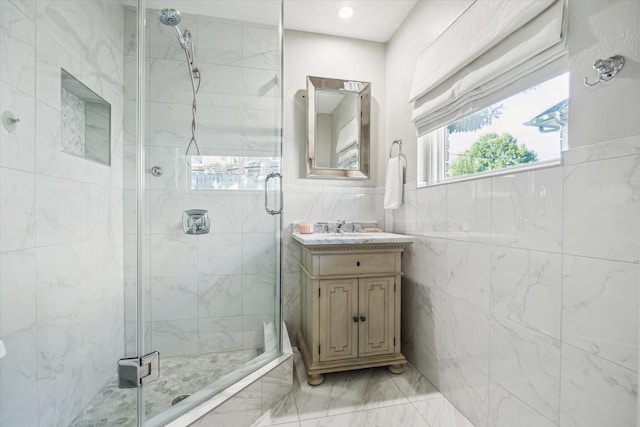 bathroom with marble finish floors, a stall shower, tile walls, vanity, and a wainscoted wall