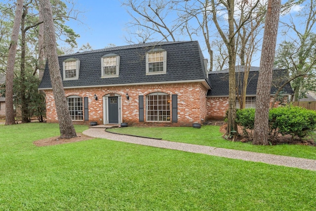view of front of house featuring a shingled roof, brick siding, mansard roof, and a front lawn