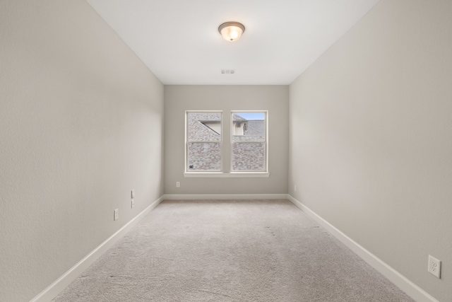 spare room featuring light carpet and baseboards