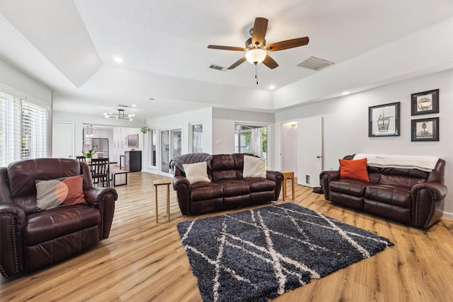 living room with a raised ceiling, light wood-style floors, a ceiling fan, recessed lighting, and a chandelier