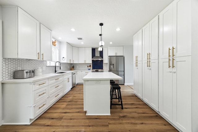 kitchen featuring wall chimney exhaust hood, appliances with stainless steel finishes, a sink, white cabinets, and a kitchen breakfast bar