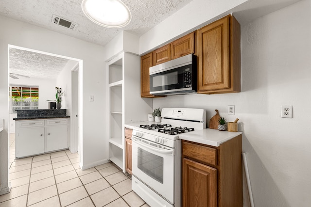 10431 Sagewillow Ln, Houston, TX 77089 - kitchen featuring white gas stove, stainless steel microwave, a textured ceiling, brown cabinetry, and light tile patterned flooring