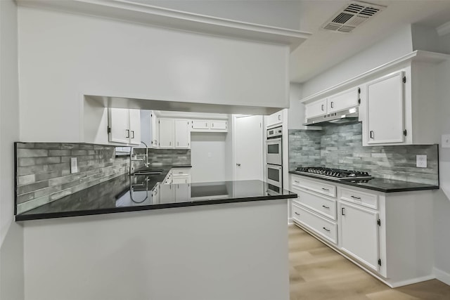 kitchen featuring dark countertops, a peninsula, backsplash, and a sink