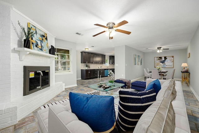 living area featuring a ceiling fan, baseboards, and a brick fireplace