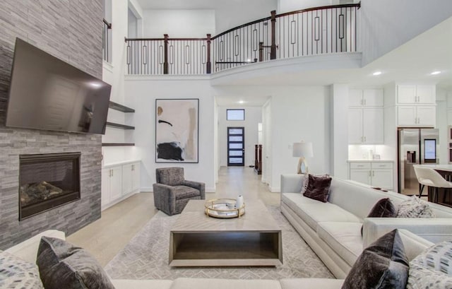 8911 Orchard Cv, Missouri City, TX 77459 - living room featuring a glass covered fireplace, recessed lighting, light wood-style flooring, a high ceiling, and baseboards