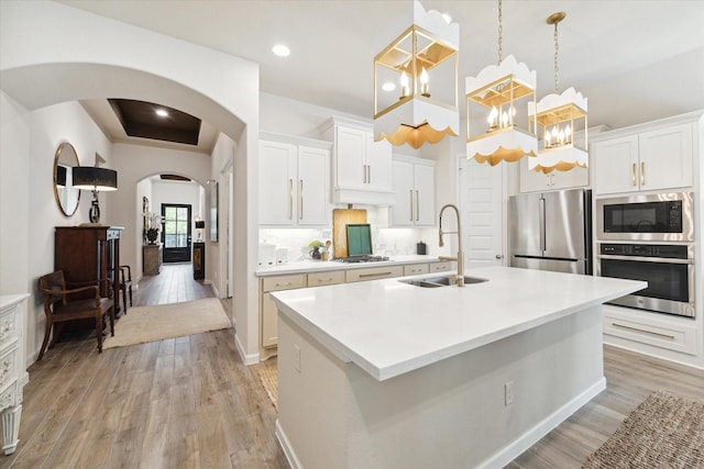 7918 Silver Grove Dr, Magnolia, TX 77354 - kitchen featuring stainless steel appliances, arched walkways, light wood-style floors, a kitchen island with sink, and light countertops