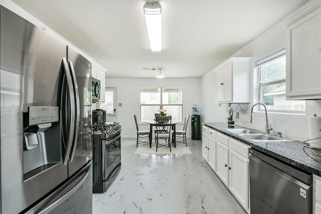 kitchen with appliances with stainless steel finishes, a sink, dark countertops, white cabinetry, and finished concrete floors