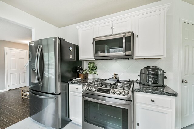 kitchen featuring appliances with stainless steel finishes, white cabinets, dark stone countertops, tasteful backsplash, and dark wood finished floors
