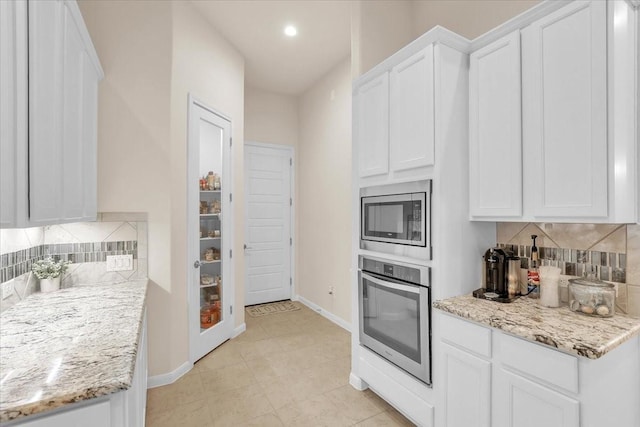 2321 Vineyard Terrace Ln, League City, TX 77573 - kitchen with appliances with stainless steel finishes, backsplash, white cabinetry, baseboards, and light stone countertops