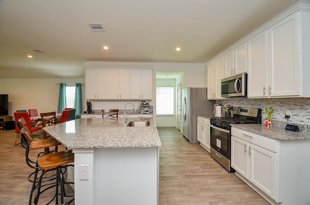 kitchen with stainless steel appliances, a sink, a kitchen bar, white cabinetry, and a kitchen island with sink