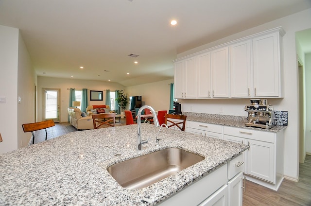 kitchen with a sink, light wood-style floors, white cabinets, recessed lighting, and light stone counters