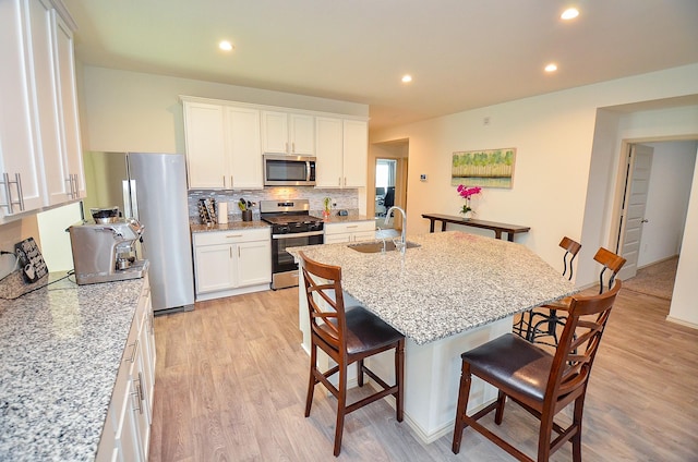 kitchen featuring appliances with stainless steel finishes, a sink, a kitchen bar, light wood-style flooring, and backsplash