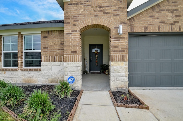 view of exterior entry featuring brick siding, a garage, and stone siding