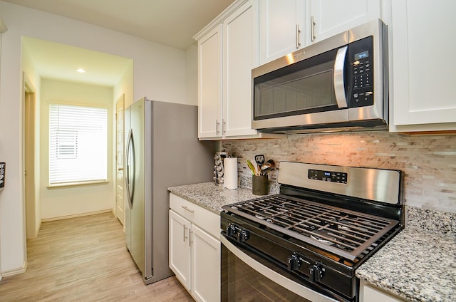 kitchen with stainless steel appliances, white cabinets, backsplash, light stone counters, and light wood finished floors