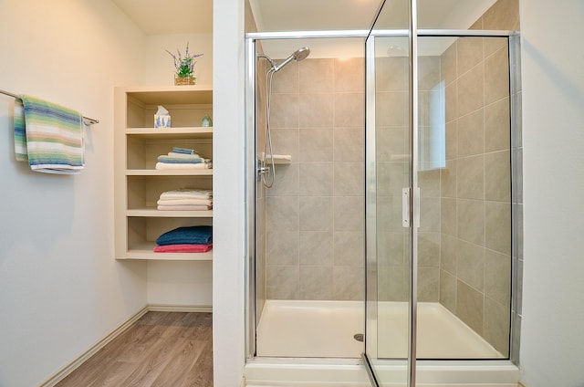 bathroom with a shower stall, wood finished floors, baseboards, and a spacious closet