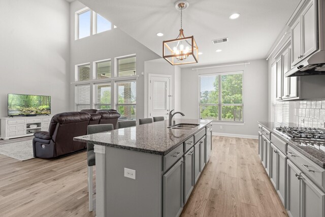 kitchen featuring a sink, stainless steel gas stovetop, a chandelier, light wood-style floors, and dark stone counters