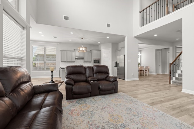 living area featuring a high ceiling, light wood-style flooring, baseboards, stairway, and recessed lighting