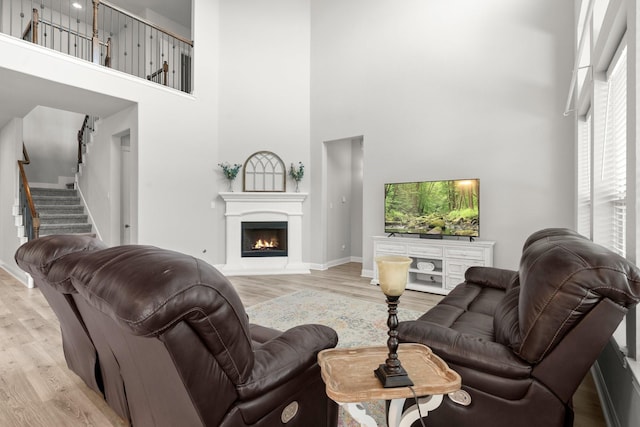 living area featuring a high ceiling, wood finished floors, baseboards, stairs, and a lit fireplace
