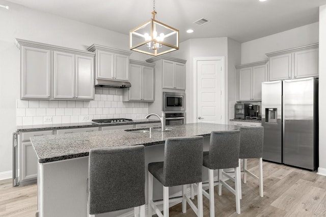 kitchen featuring appliances with stainless steel finishes, a sink, under cabinet range hood, gray cabinets, and a breakfast bar