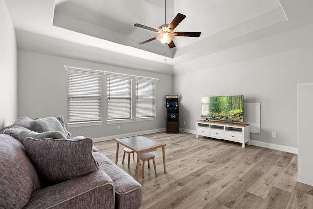 living room with a raised ceiling, ceiling fan, light wood-style flooring, and baseboards