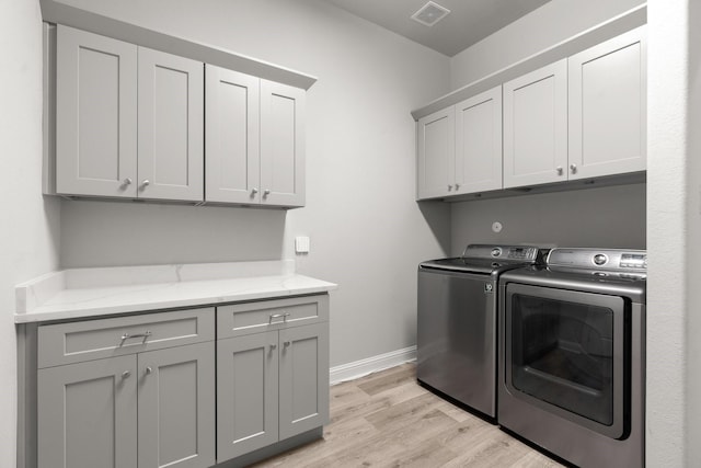clothes washing area featuring cabinet space, separate washer and dryer, light wood-style flooring, and baseboards