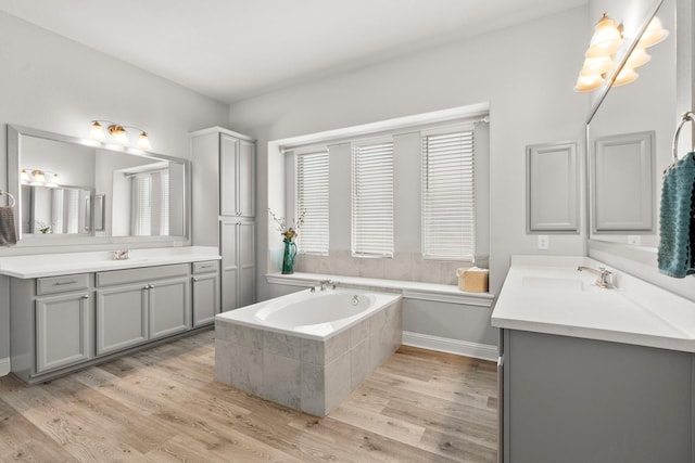 bathroom with wood finished floors, a bath, and two vanities