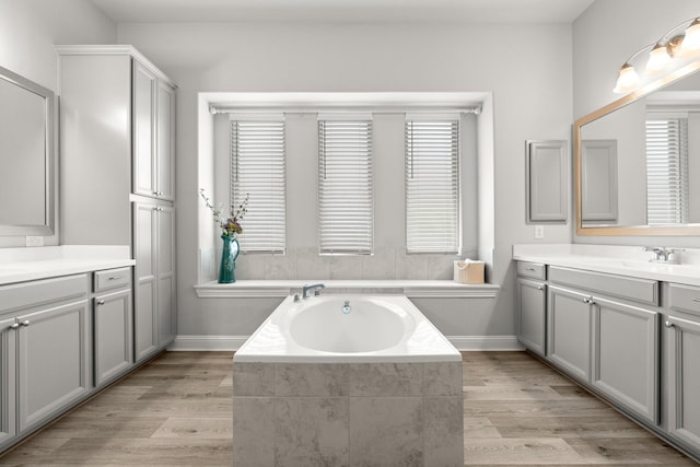 bathroom with a garden tub, vanity, wood finished floors, and baseboards