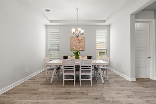 dining room with a chandelier, wood finished floors, baseboards, and a tray ceiling