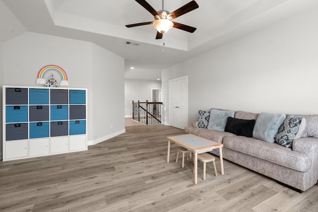 living area featuring a tray ceiling, light wood-type flooring, a ceiling fan, baseboards, and recessed lighting