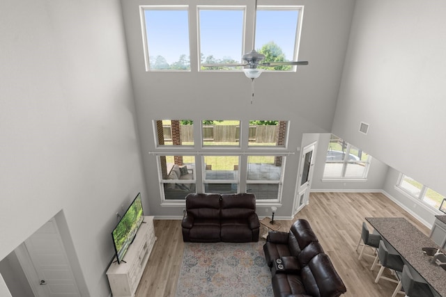 living area with a towering ceiling, wood finished floors, baseboards, and ceiling fan
