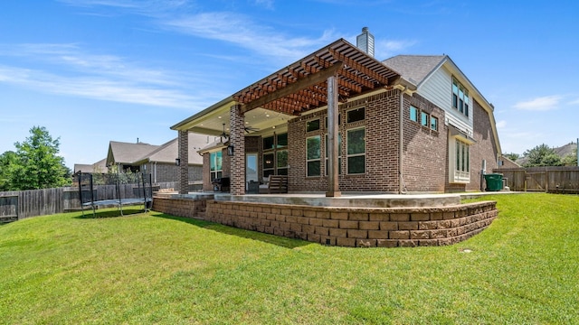 rear view of property with a trampoline, brick siding, a patio, a chimney, and ceiling fan