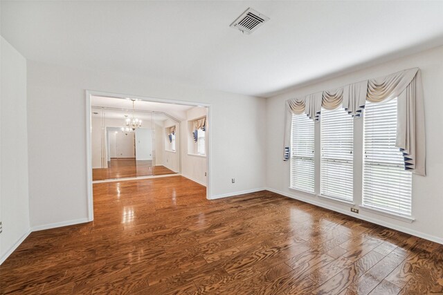 empty room featuring a chandelier, healthy amount of natural light, wood finished floors, and baseboards
