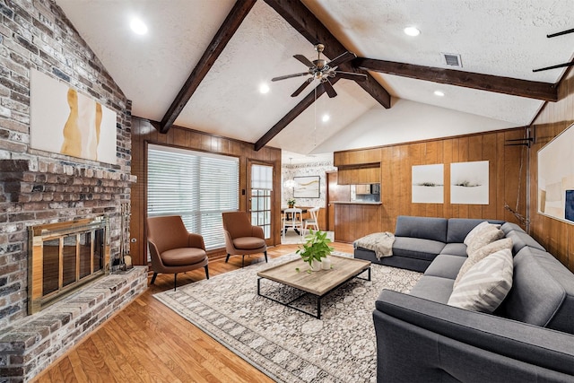 living room featuring wood walls, a brick fireplace, light wood-type flooring, a ceiling fan, and recessed lighting