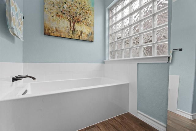 bathroom featuring a garden tub, wood finished floors, and a textured wall
