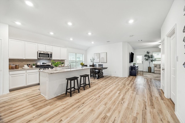 kitchen with stainless steel appliances, white cabinetry, light wood-style flooring, recessed lighting, and a center island with sink