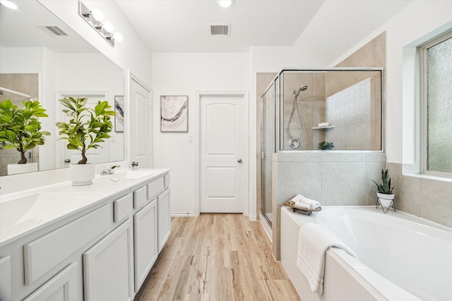 full bathroom featuring a shower stall, a bath, wood finished floors, and double vanity