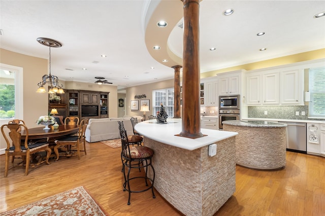 23303 Holly Creek Trl, Tomball, TX 77377 - kitchen featuring a center island, ornate columns, appliances with stainless steel finishes, crown molding, and light wood-style flooring