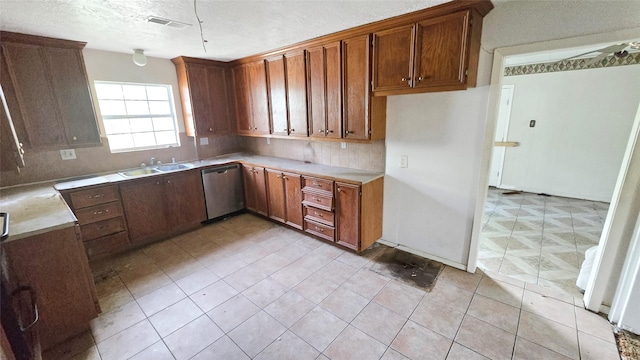 kitchen featuring stainless steel dishwasher, a sink, backsplash, light countertops, and brown cabinetry
