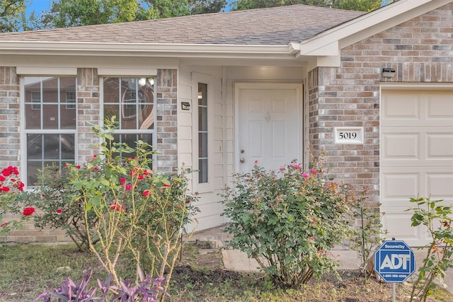 property entrance with an attached garage, roof with shingles, and brick siding