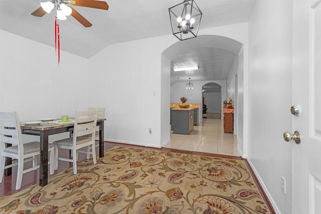 dining space with arched walkways, a ceiling fan, vaulted ceiling, baseboards, and a chandelier