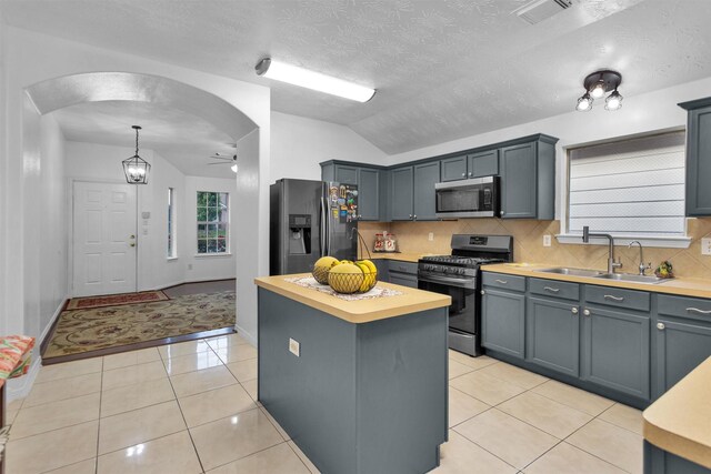 kitchen with appliances with stainless steel finishes, a sink, backsplash, arched walkways, and lofted ceiling