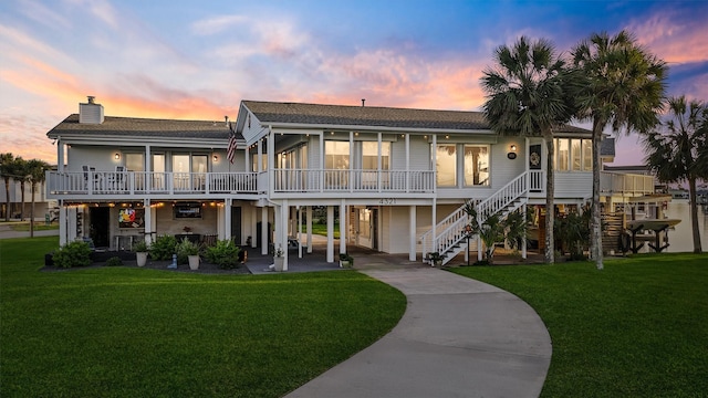 4321 Jolly Roger Rd, Galveston, TX 77554 - back of house at dusk featuring a chimney, a lawn, stairway, a shingled roof, and concrete driveway