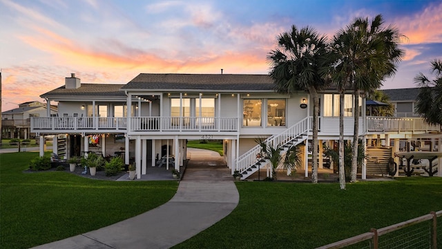 4321 Jolly Roger Rd, Galveston, TX 77554 - back of property at dusk with stairway, a yard, and a shingled roof