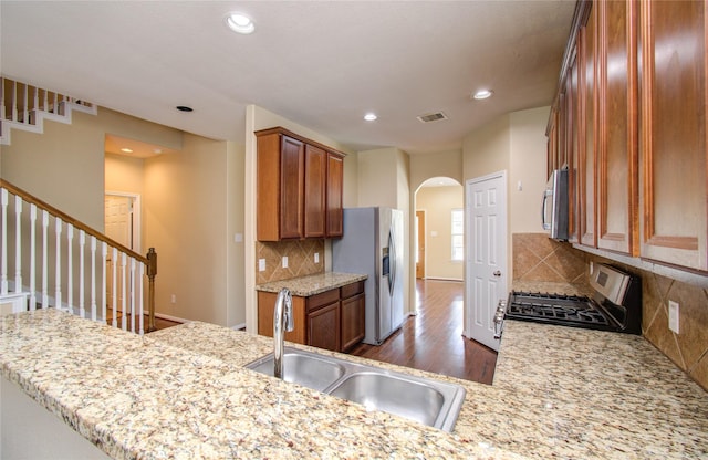 17607 Memorial Falls Dr, Tomball, TX 77375 - kitchen with stainless steel appliances, a sink, arched walkways, dark wood-style floors, and brown cabinets