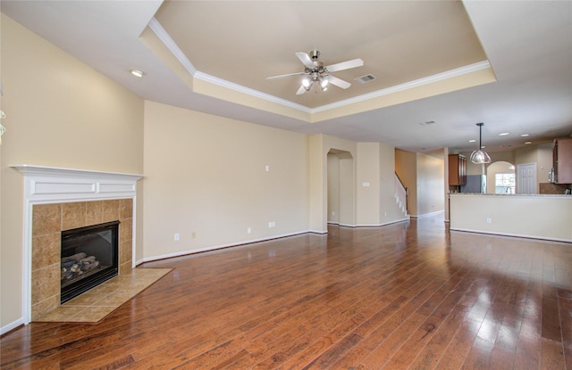 17607 Memorial Falls Dr, Tomball, TX 77375 - unfurnished living room featuring a tray ceiling, crown molding, a fireplace, ceiling fan, and dark wood-style floors