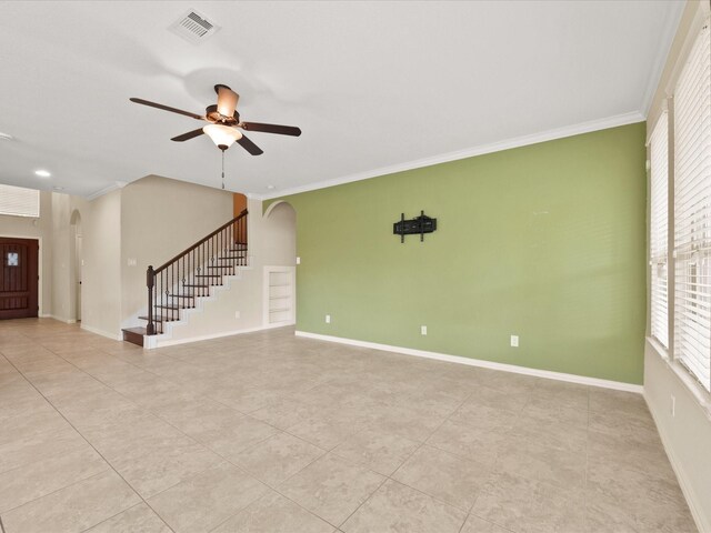 unfurnished living room with arched walkways, stairs, tile patterned floors, ornamental molding, and ceiling fan