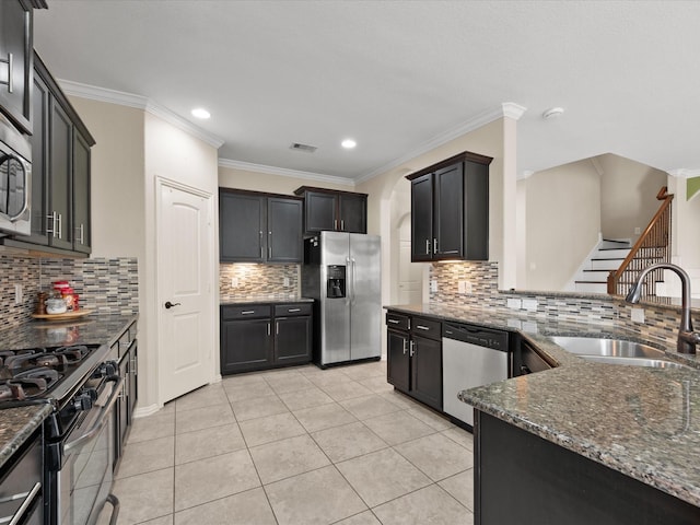 kitchen featuring stainless steel appliances, a sink, decorative backsplash, dark stone countertops, and crown molding
