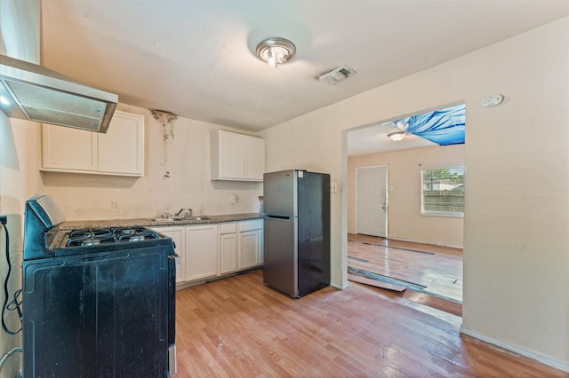 kitchen featuring freestanding refrigerator, gas stove, light wood-style flooring, a sink, and white cabinetry