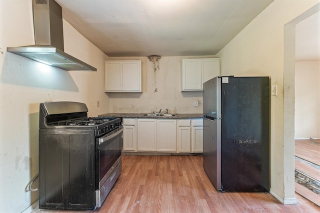 kitchen with stainless steel appliances, wall chimney exhaust hood, light wood-style flooring, and white cabinets